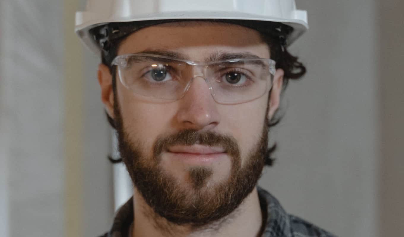 a person wearing glasses, with a hard hat, and beard smiling for the camera